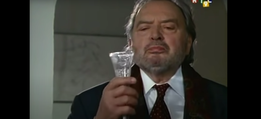 Robert Schreiber dans l'épisode de Derrick: La fin du voyage, tenant une coupe de champagne